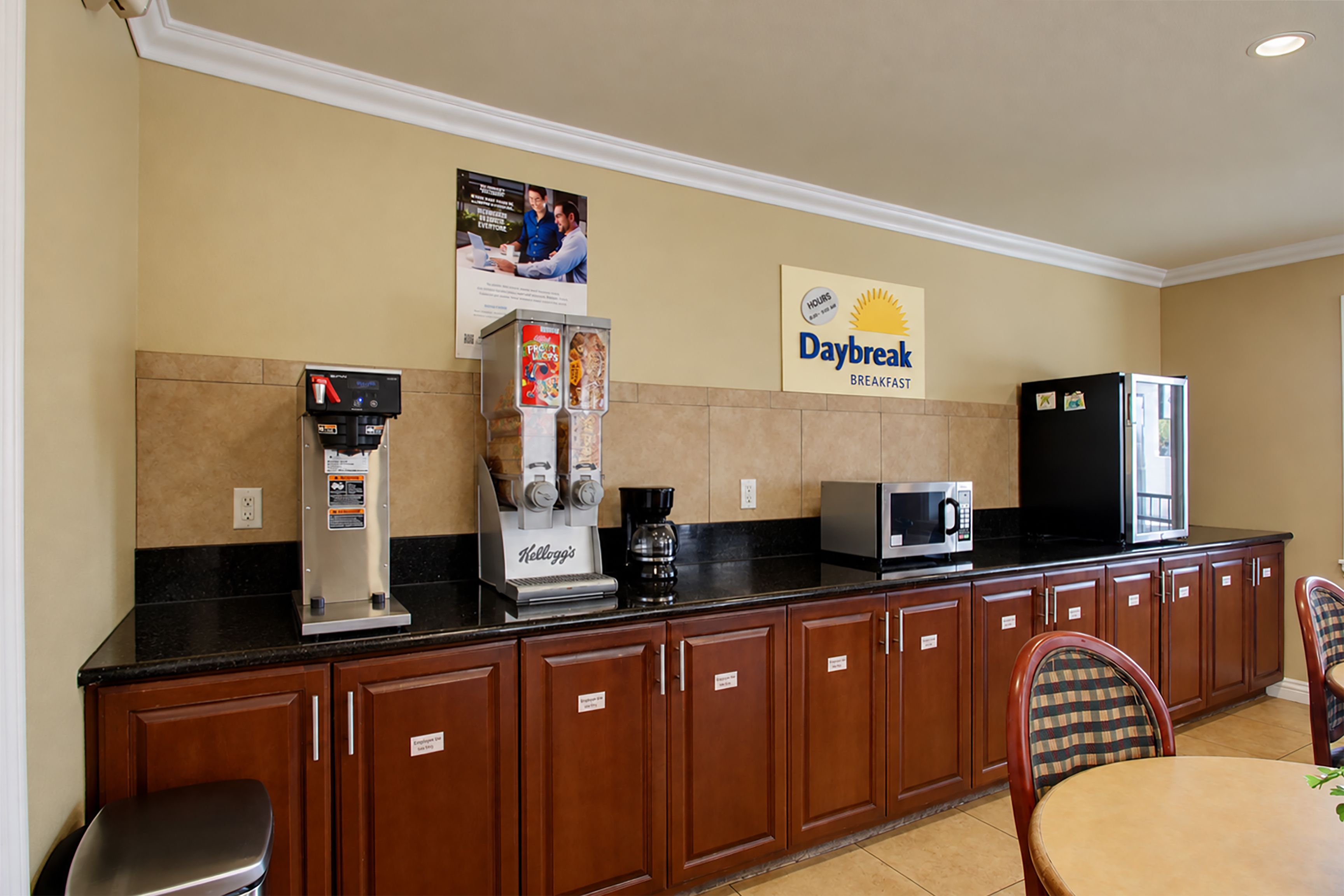 A hotel breakfast area with a coffee machine, a refrigerator, a microwave, and a sign for Daybreak breakfast.