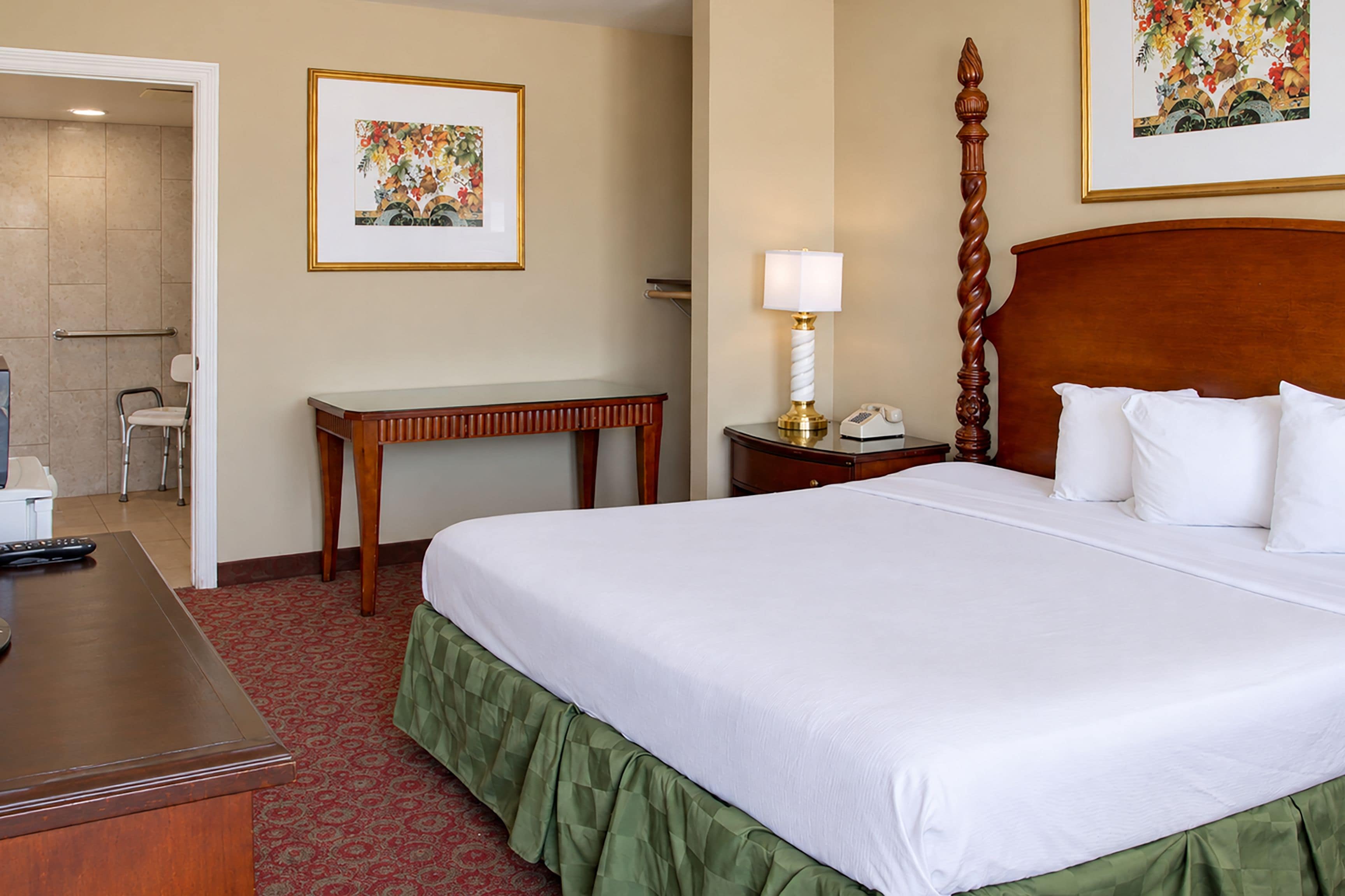 A hotel room with a large bed, a bedside table, a lamp, a chair, and a small table.