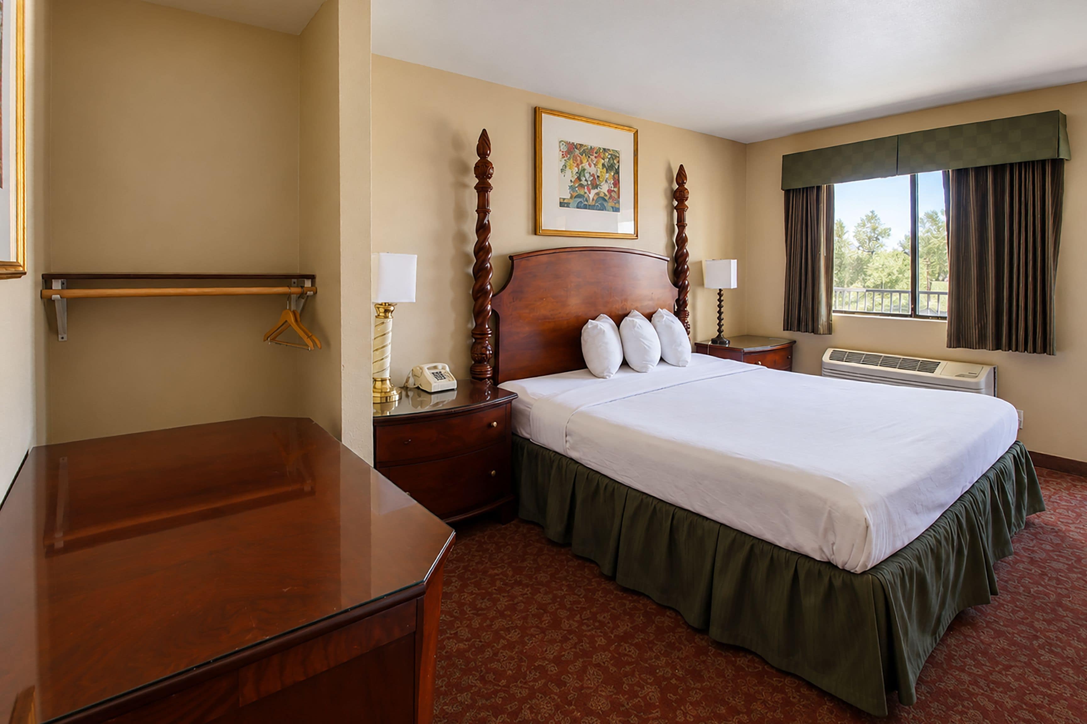 A hotel room with a large bed, a bedside table with a lamp, a dresser, a window with curtains, and a painting on the wall.