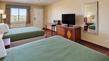 A hotel room with two beds, a television, a desk, and a window with curtains.