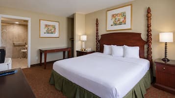 A hotel room with a large bed, a desk, a chair, a bedside table, a lamp, and a picture frame on the wall.