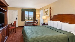 A hotel room with a large bed, a desk, a chair, a television, and a window with a mountain view. - Kingman Inn Route 66 I-40 (Kingman)