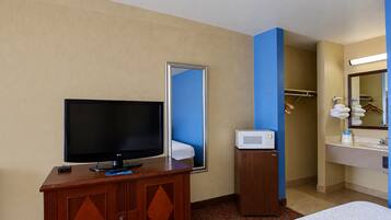 A hotel room with a television on a wooden cabinet, a microwave, a bathroom with a sink and mirror, and a bed with a white comforter.