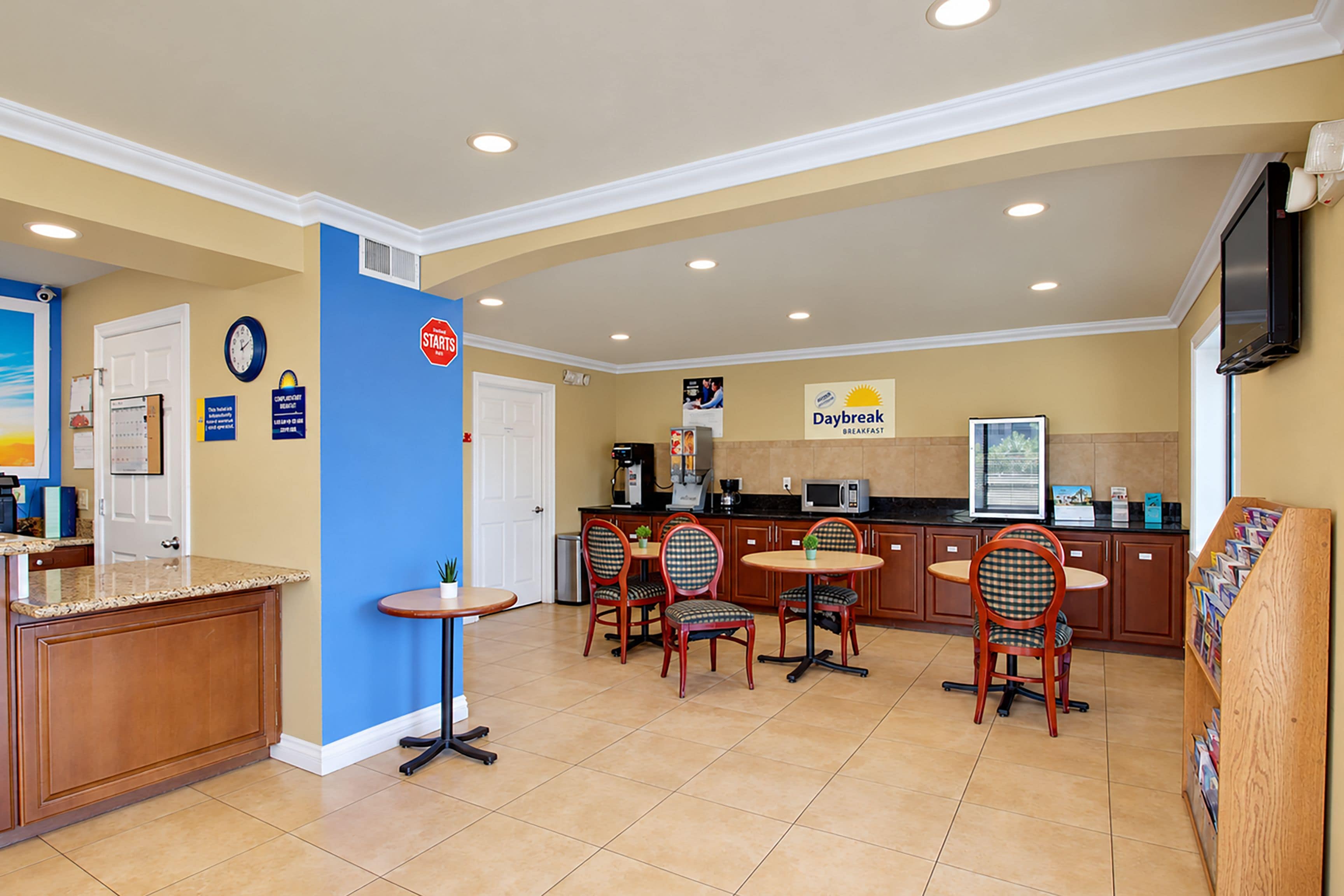 A hotel breakfast area with a counter, seating, a clock, and a Daybreak sign.