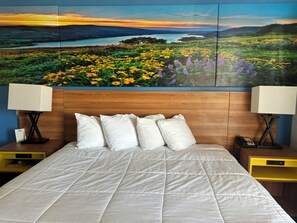 A hotel room with a large bed, white bedding, and a wooden headboard. There are two bedside tables with lamps and a nightstand with a phone.