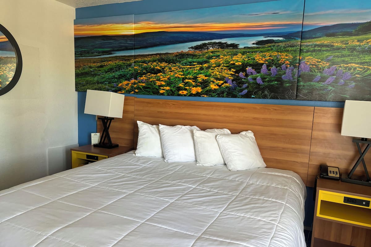 A bed with white bedding, a wooden headboard, and a nightstand with a lamp.