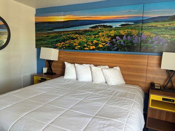 A bed with white bedding, a wooden headboard, and a nightstand with a lamp.