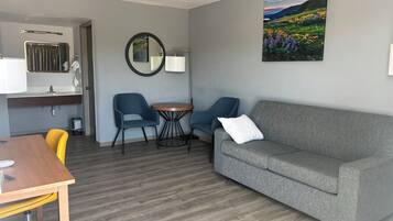 Ein modernes Wohnzimmer mit einem grauen Sofa, zwei blauen Sesseln, einem Holzesstisch und einem kleinen runden Tisch mit einer Lampe.