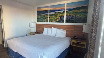 Ett hotellrum med en stor säng, två sängbord, ett litet bord och en tavla som hänger på väggen.