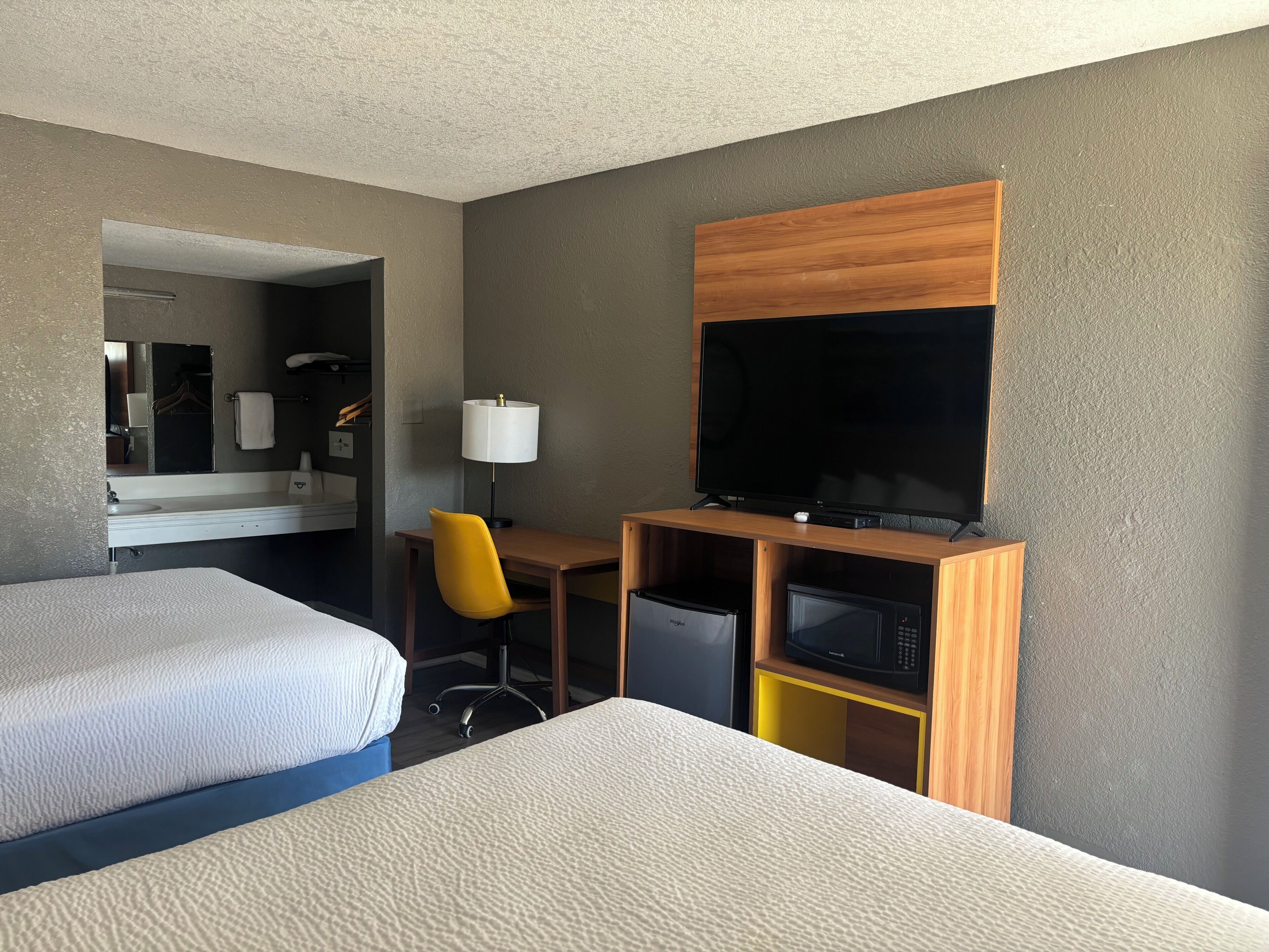 A hotel room with two beds, a desk with a chair, a television, and a microwave.