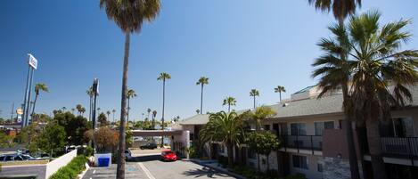 A parking lot with a red car, palm trees, and a building with a balcony.