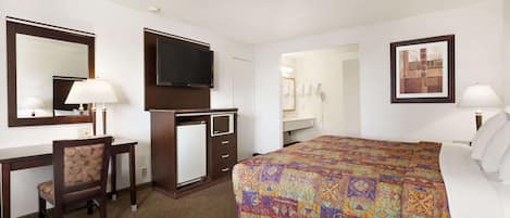 A hotel room with a bed, a desk with a chair, a television, a mirror, and a bathroom visible through an open door.