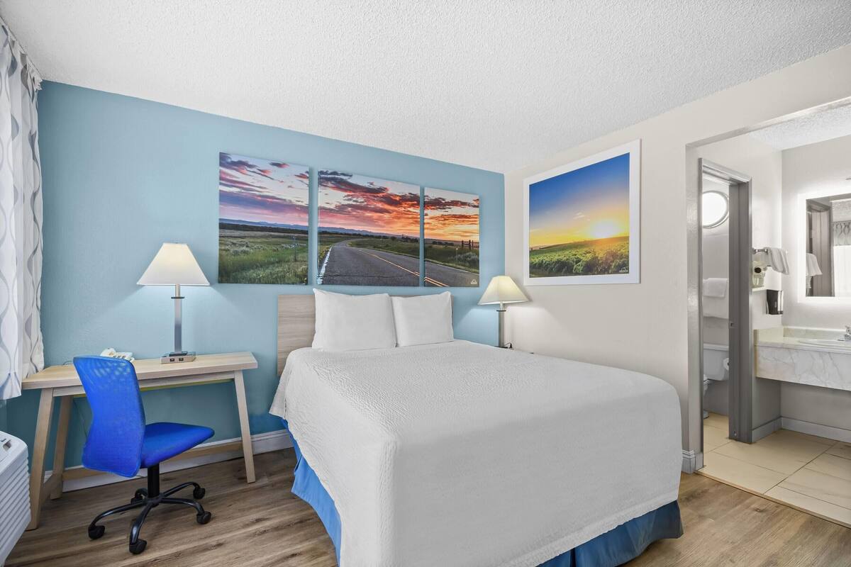 A hotel room with a bed, desk, chair, and two wall-mounted lamps.