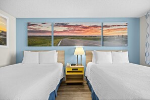 A hotel room with two beds, a nightstand with a lamp, and a wall with three landscape paintings.