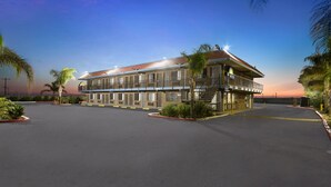 A two-story building with a balcony and a covered walkway, surrounded by palm trees and a parking lot. - Days Inn by Wyndham Lost Hills (Lost Hills)