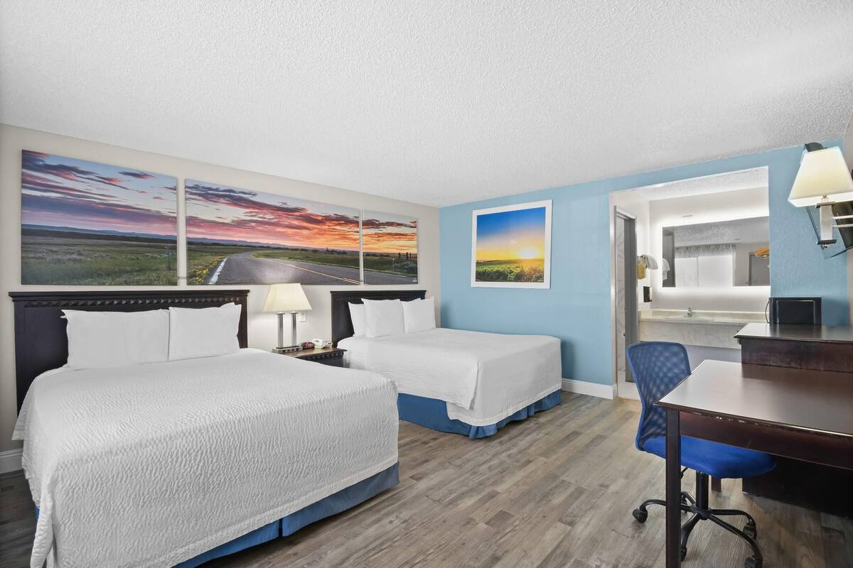 A hotel room with two beds, a desk, a chair, and a large window.
