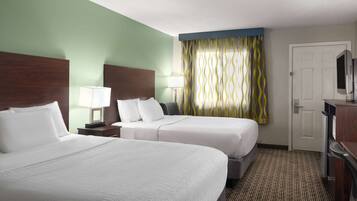 A hotel room with two beds, a desk, a TV, and a door.