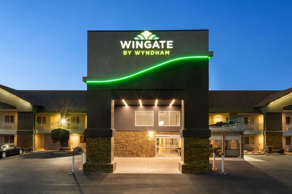 Entrada d'hotel amb un cartell que diu 'Wingate by Wyndham', un aparcament i un edifici amb diversos balcons.