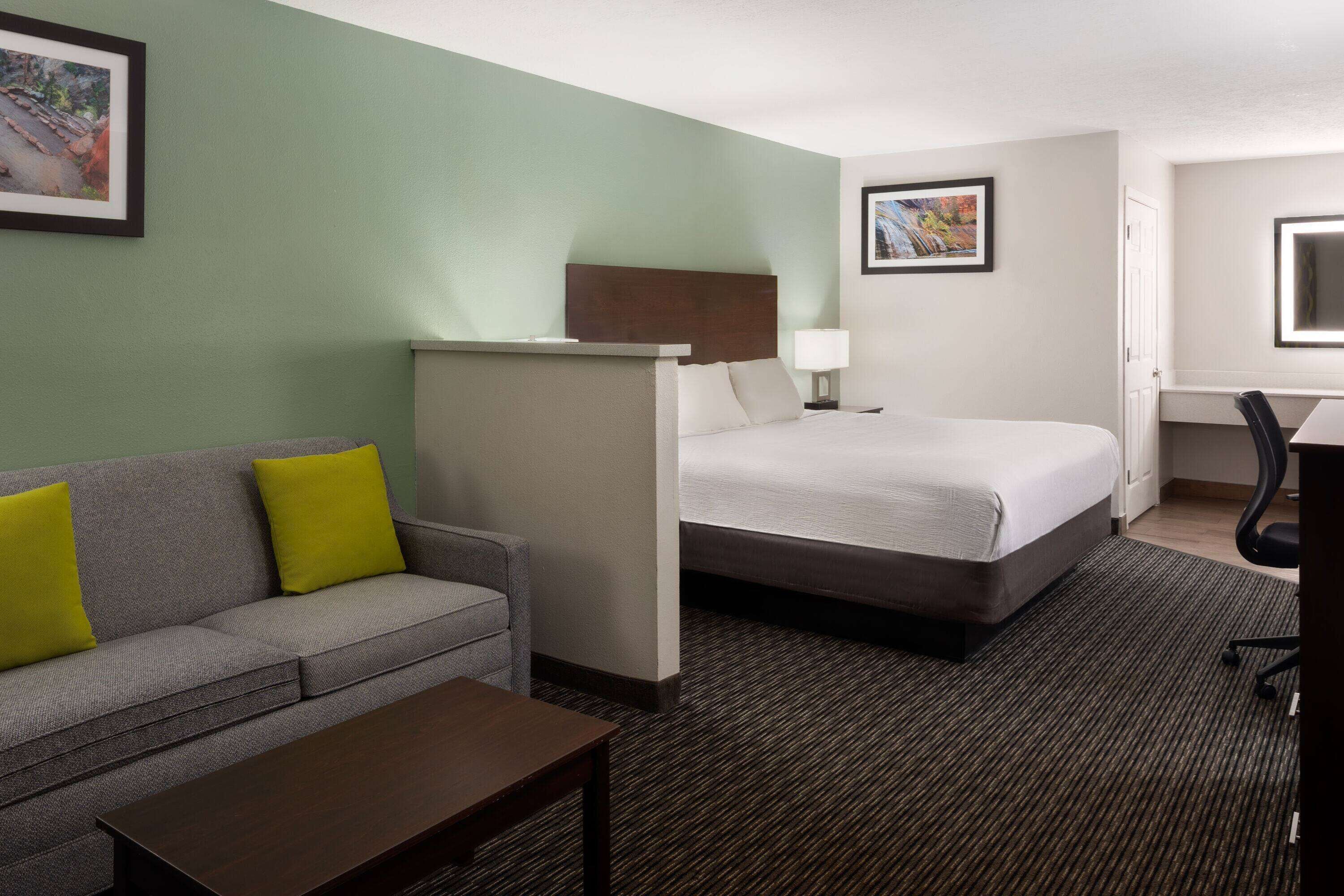 A hotel room with a bed, a sofa with yellow cushions, a desk, and a chair.