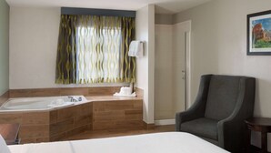 Een hotelkamer met een groot bad, een douche, een stoel en een schilderij aan de muur.