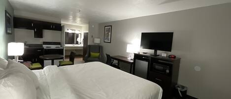 Een hotelkamer met een bed, bureau, stoel, televisie en kitchenette.