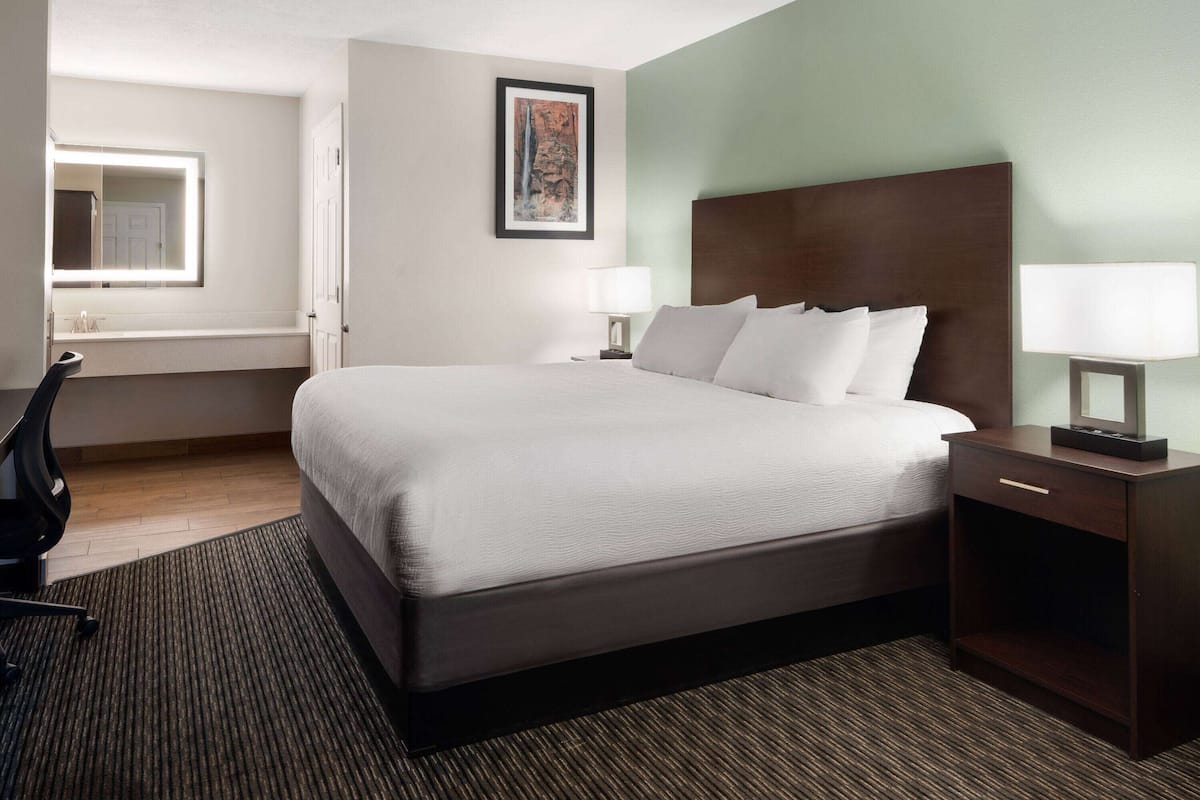 Una habitación de hotel con una cama grande, dos mesitas de noche con lámparas, un escritorio y una silla.