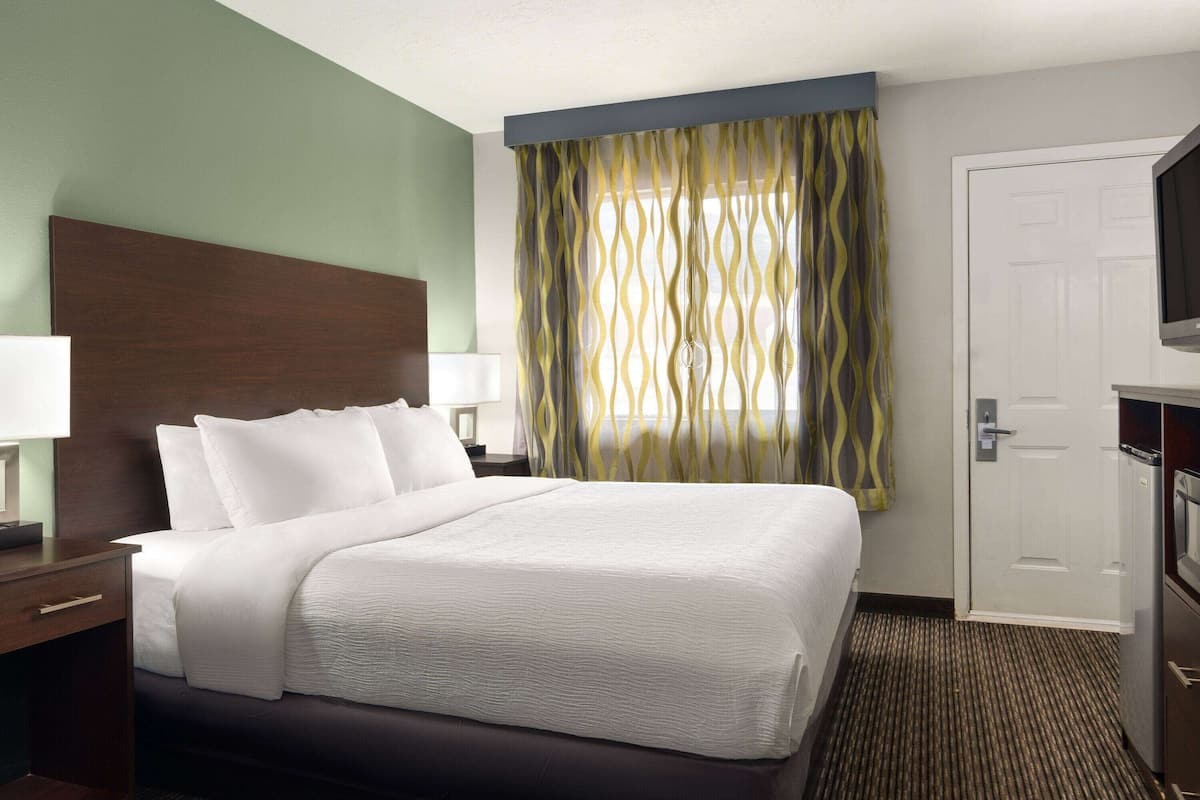 Una habitación de hotel con una cama grande, un cabecero de madera, dos mesitas de noche con lámparas, un televisor y una puerta.