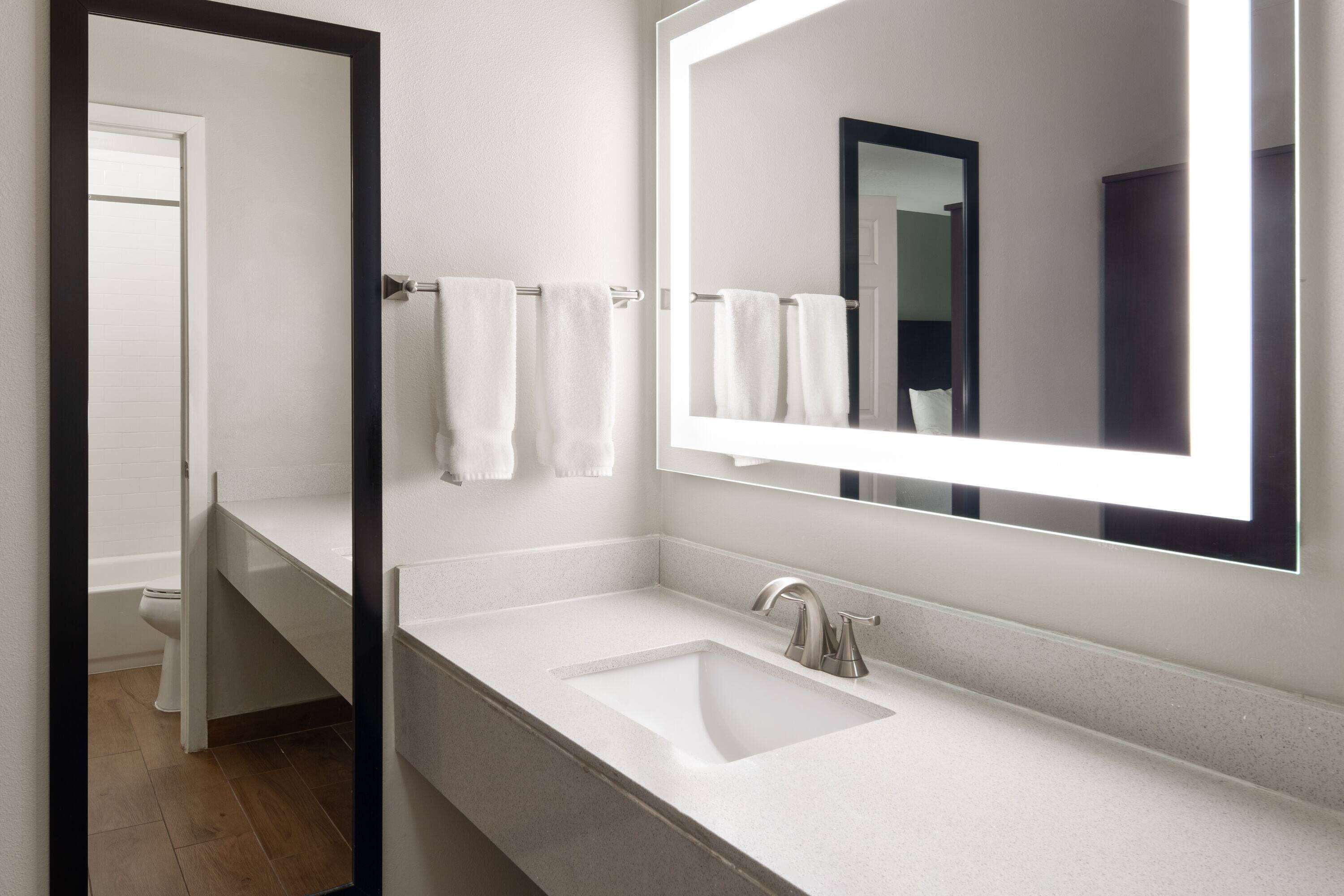 A modern bathroom with a white sink, a large mirror, and a towel rack.