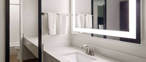 A modern bathroom with a white sink, a large mirror, and a towel rack.