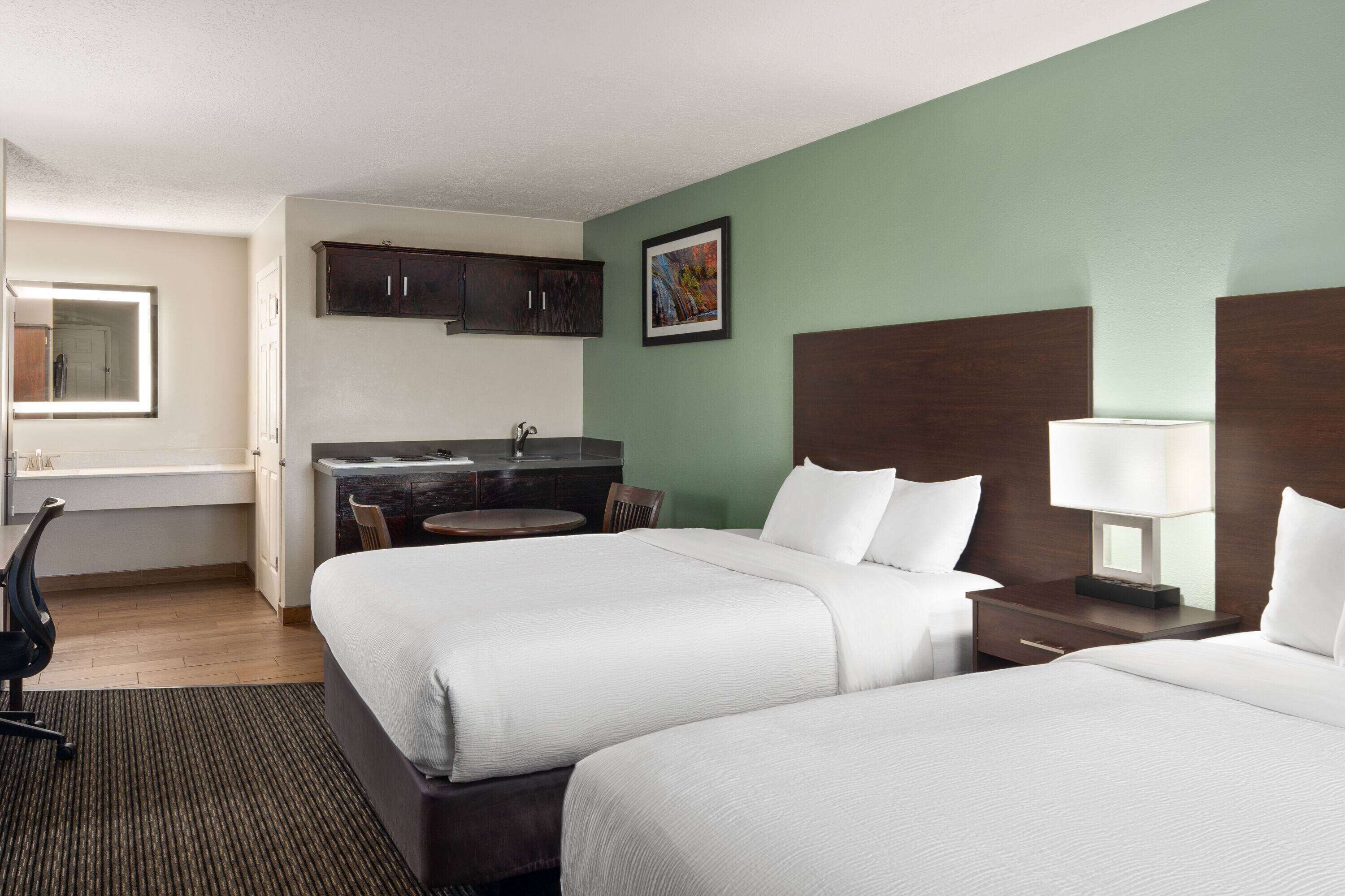 A hotel room with two beds, a desk, a chair, a sink, and a mirror.