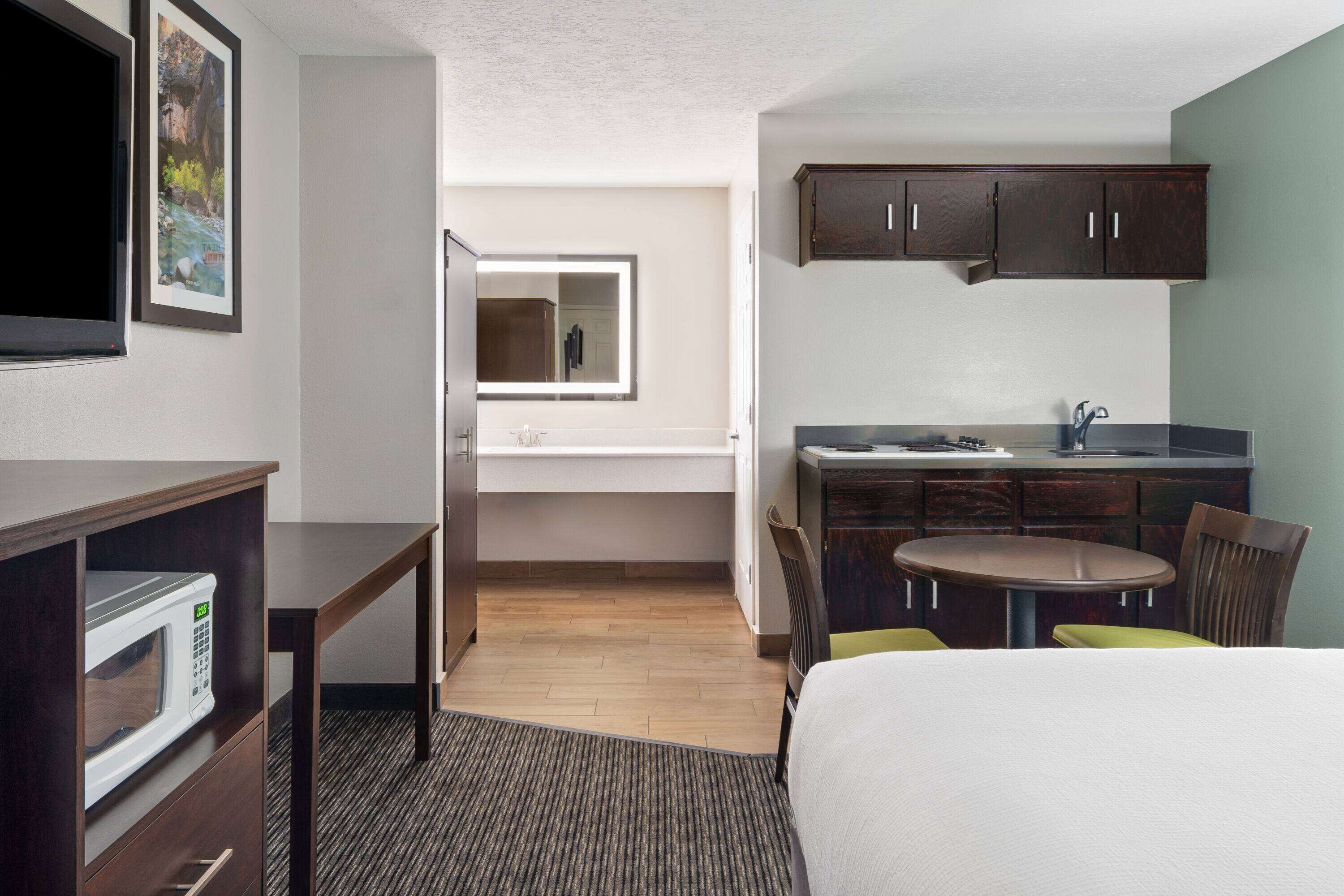 Ein Hotelzimmer mit einem Bett, einem Schreibtisch mit Mikrowelle, einem kleinen Esstisch mit Stühlen, einem Waschbecken und Schränken.