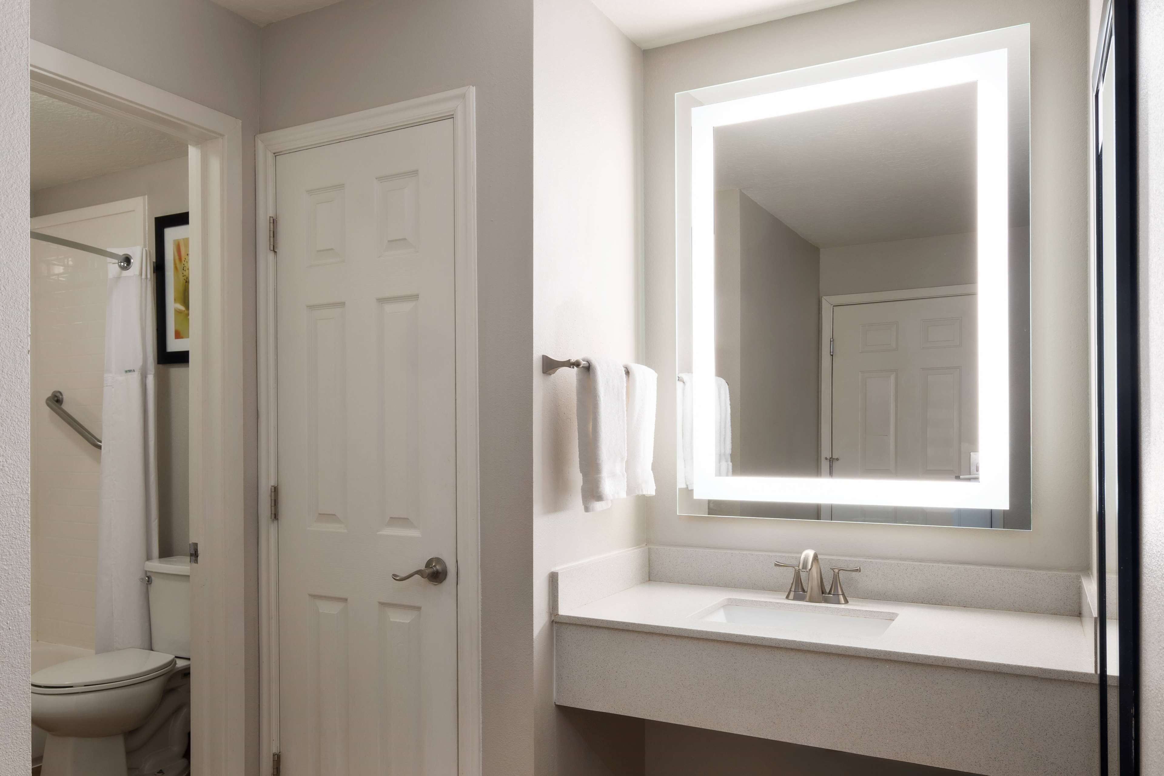 Un baño con inodoro blanco, lavamanos y espejo superior, y una puerta.