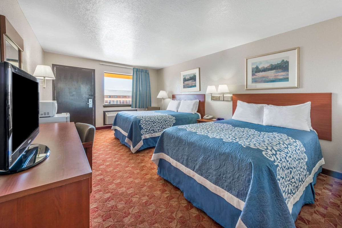 A hotel room with two beds, a desk with a television, and a window with curtains.