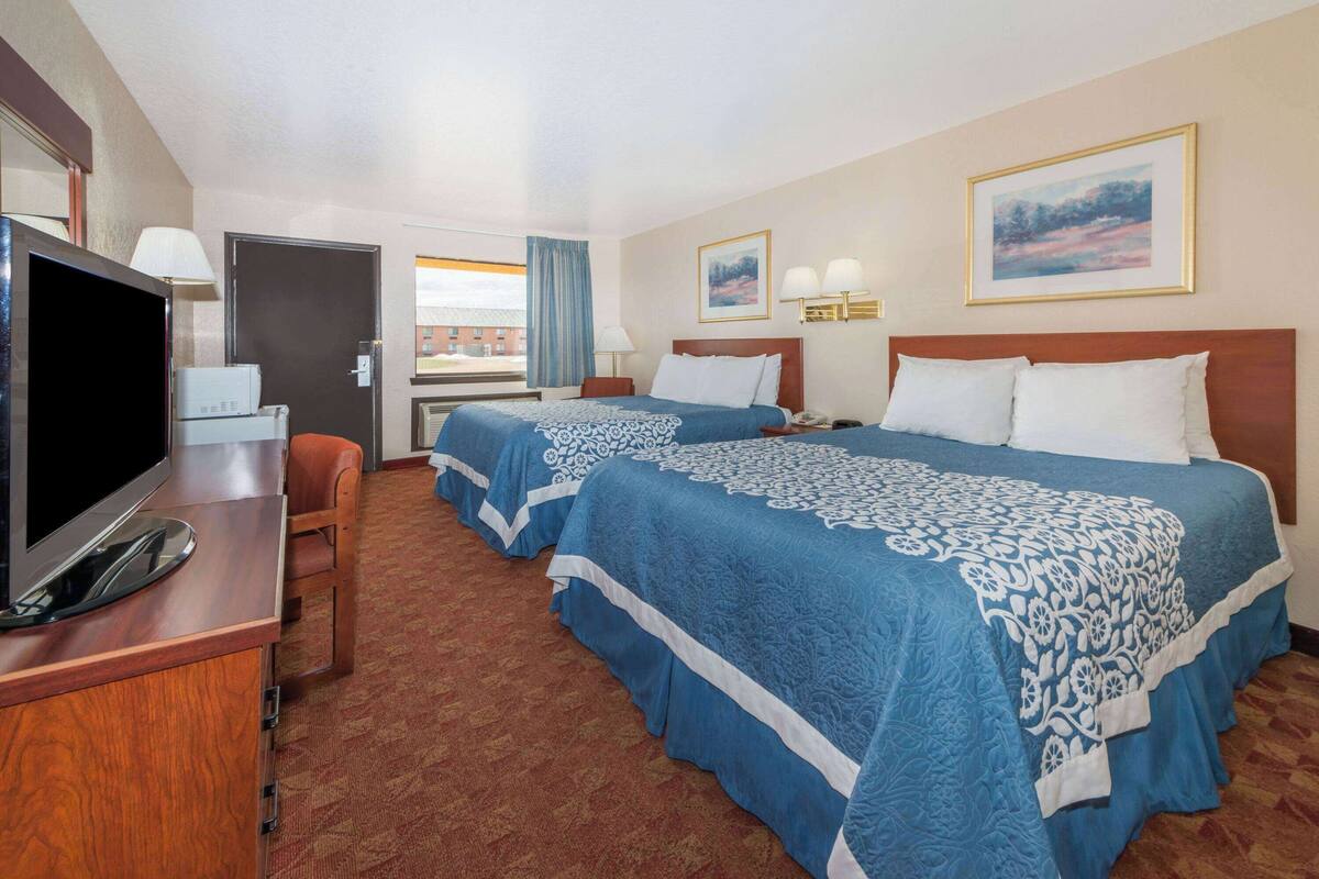 A hotel room with two beds, a TV, a desk, and a window with a view.