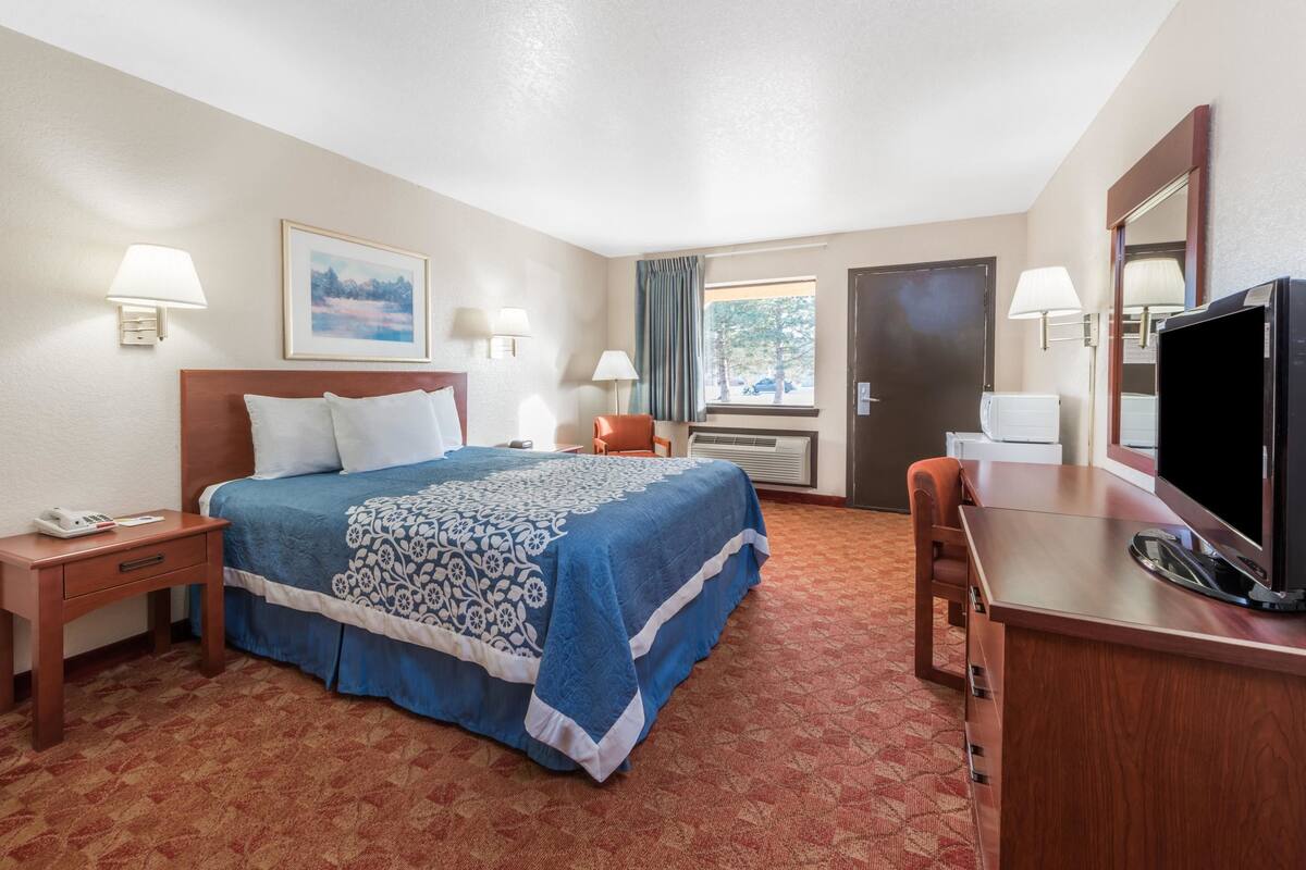 A hotel room with a bed, a desk, a television, and a window with curtains.
