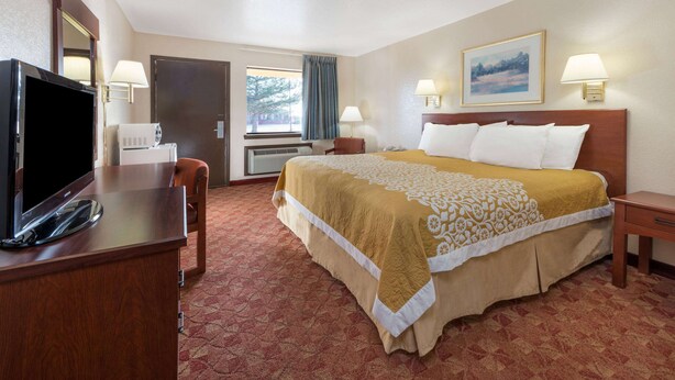A hotel room with a bed, a desk with a TV, a window with curtains, and two bedside lamps.