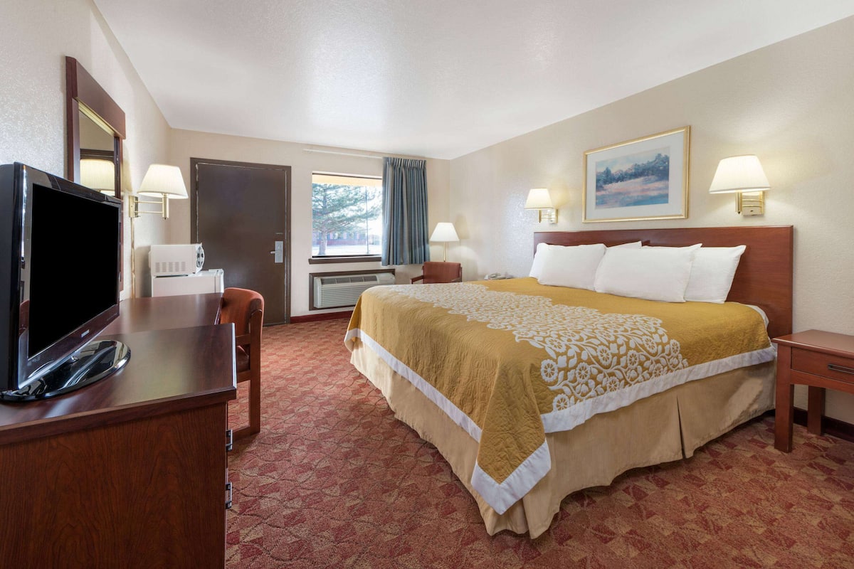 A hotel room with a bed, a desk with a TV, a window with curtains, and two bedside lamps.