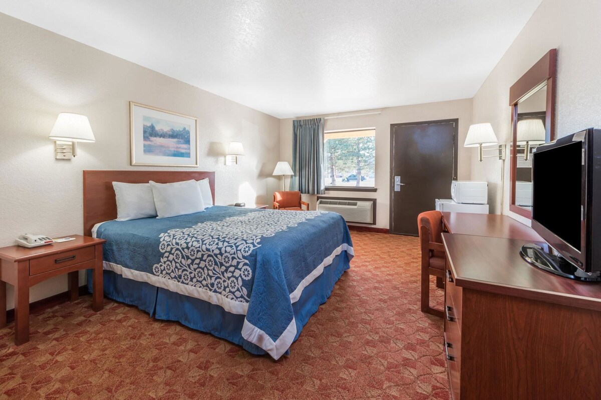 Habitación de hotel con cama, escritorio con televisor, una silla, ventana con cortinas y puerta.