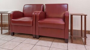 A pair of red leather armchairs with wooden side tables, placed on a tiled floor against a plain wall.