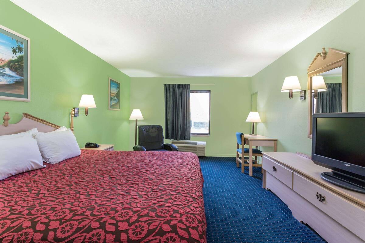 Ein Hotelzimmer mit Bett, Schreibtisch, Fernseher und einem Fenster mit Vorhängen.