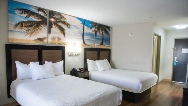 A hotel room with two beds, wooden headboards, a nightstand, a lamp, and a beach-themed wall mural.