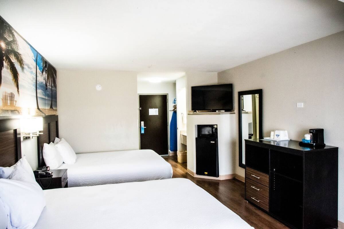 Ein Hotelzimmer mit zwei Betten, einem Fernseher, einer Minibar, einem Spiegel und einem Bild an der Wand.