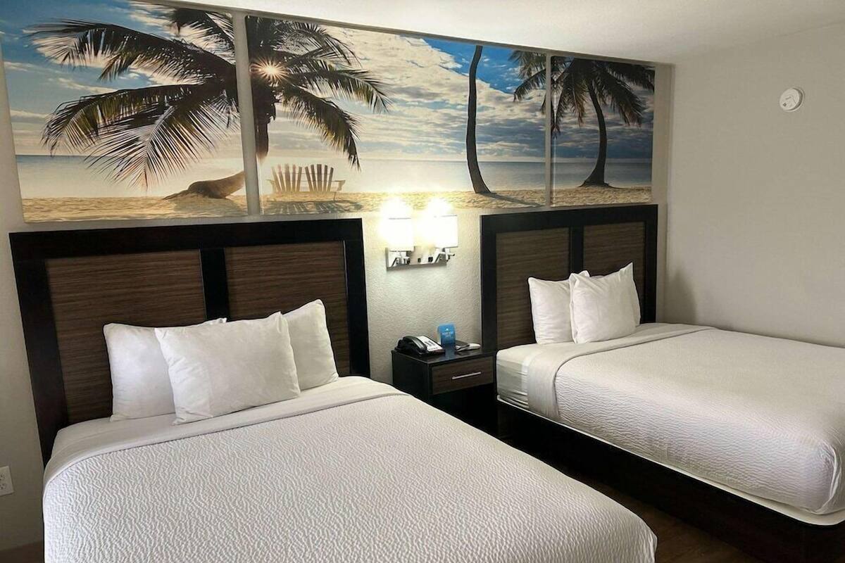 Ein Hotelzimmer mit zwei Betten, einem Nachttisch, einer Wandlampe und einem Wandbild mit Strandmotiv.