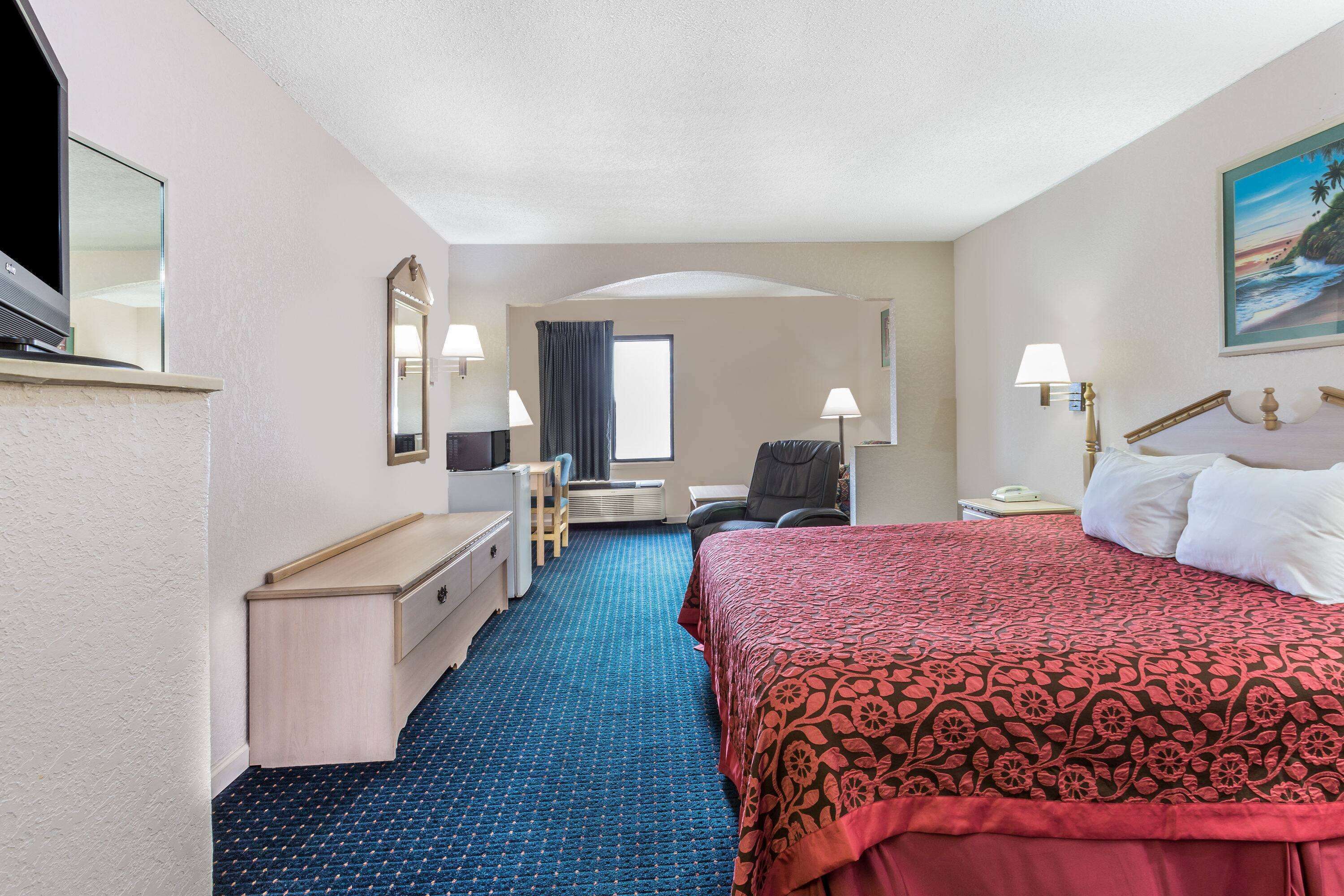 A hotel room with a bed, desk, chair, and a large window.