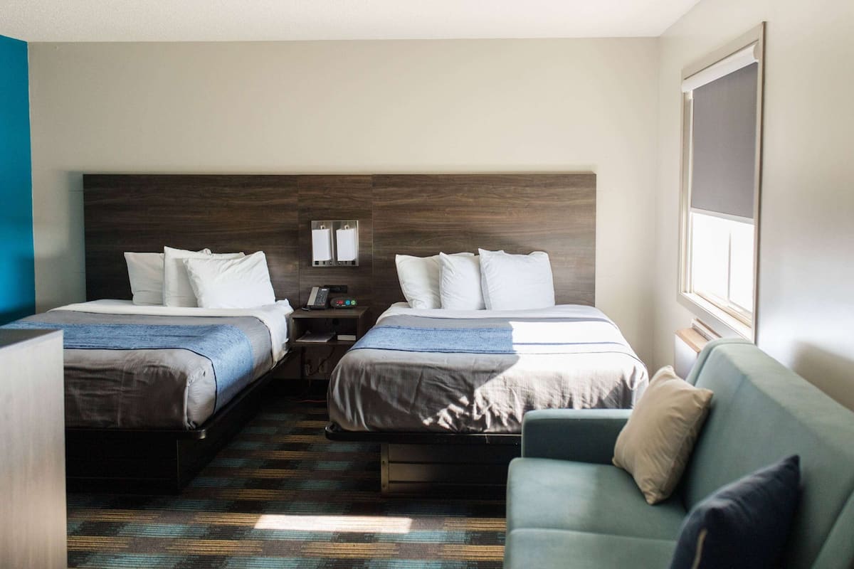 Habitación de hotel con dos camas, un sofá, una mesita y un ventanal.