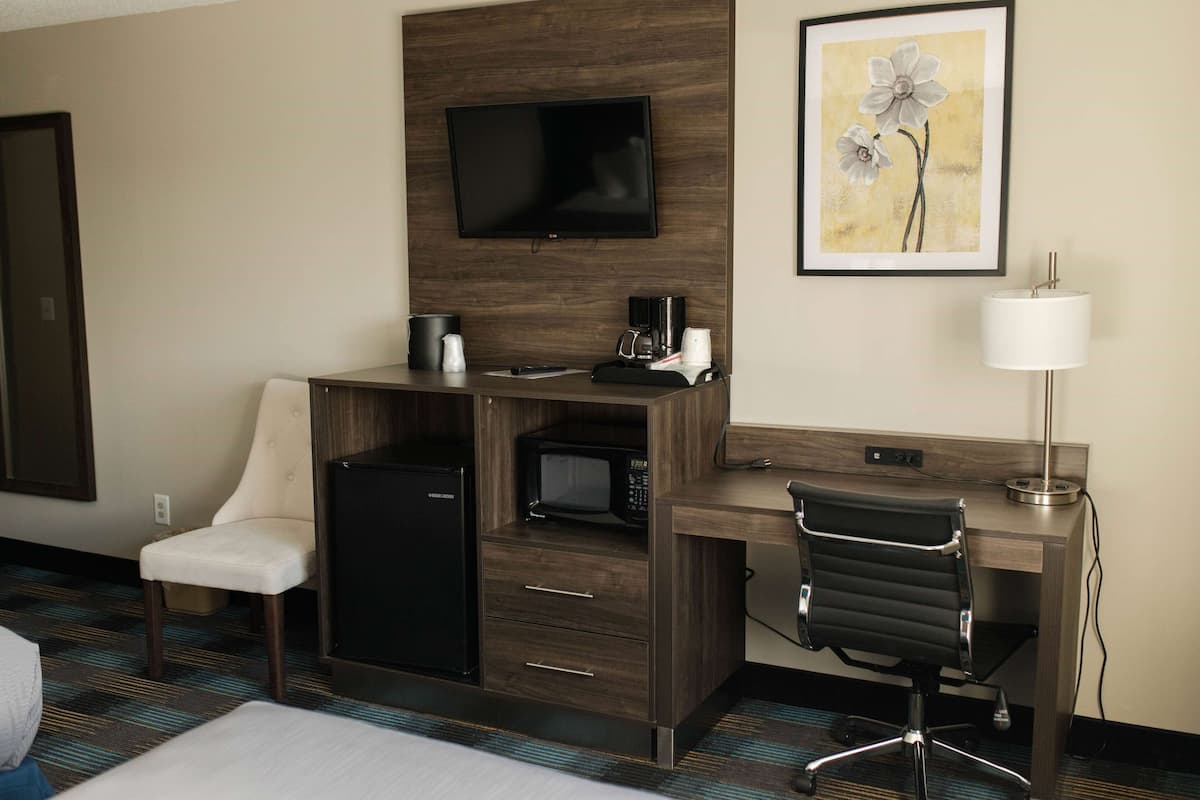 Habitación de hotel con escritorio, silla, televisión, microondas, refrigerador y una cama.