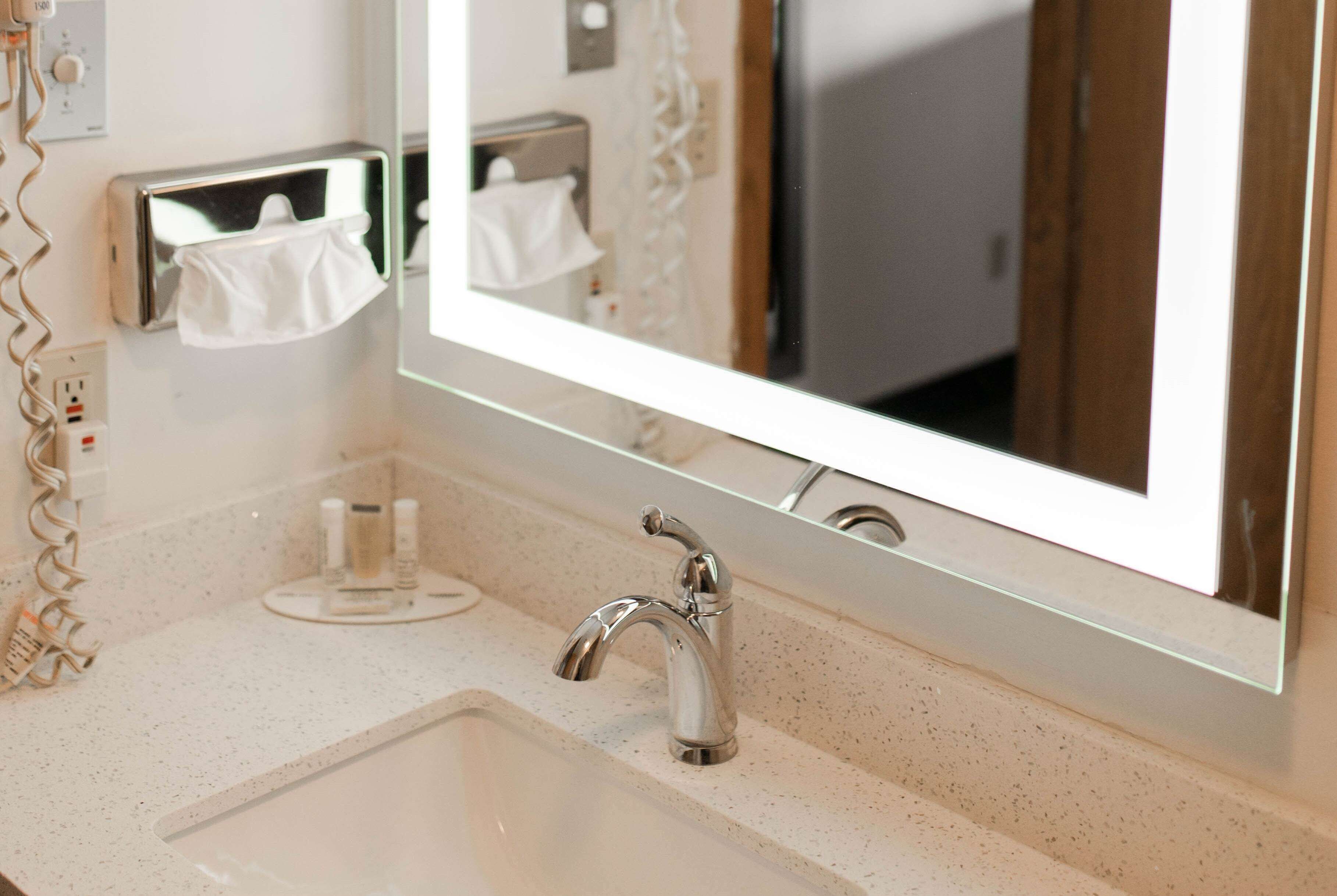 A bathroom with a large mirror, a sink, and a towel dispenser.