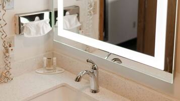A bathroom with a large mirror, a sink, and a towel dispenser.