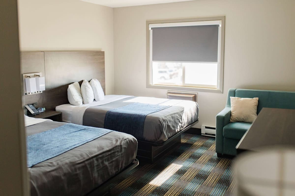 Habitación de hotel con dos camas, un escritorio, una silla y ventana con vistas.