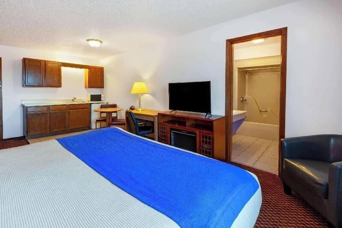 Habitación de hotel con cama, escritorio con silla, televisor, baño con ducha y armarios de madera.